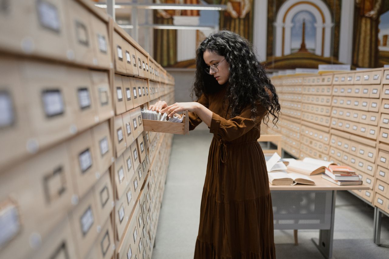 Home A woman browsing a card catalog in library archives, focusing on research and information gathering.